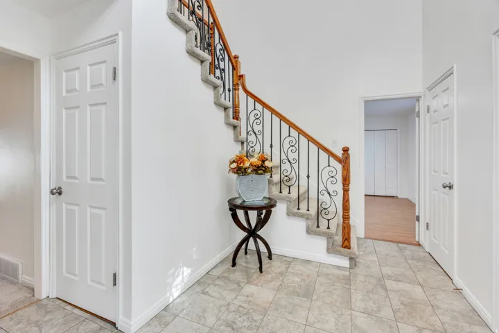 Foyer with marble tiled entryway flooring, staircase with carpeted treads, wrought iron balusters, wood handrail, and white paneled doors