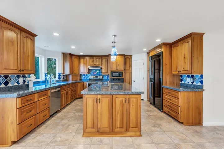 Kitchen featuring wood cabinetry, a central island, granite-style countertops, and stainless steel appliances