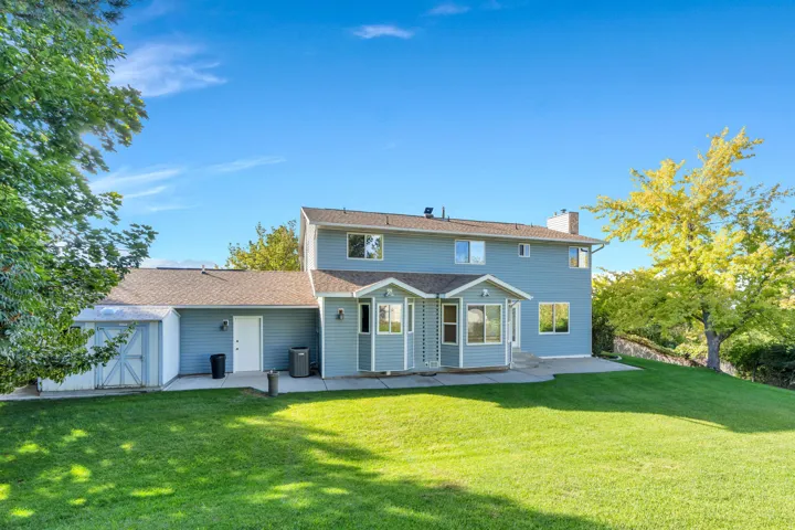 Backyard .35 Acre, Expansive green lawn with a sloped grade, concrete patio area, light blue exterior siding, and a detached shed structure