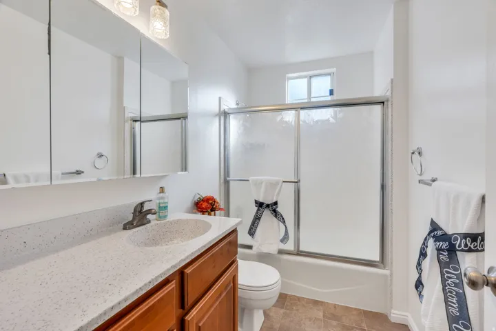 Hall bathroom with tub/shower, vanity with a speckled countertop and an integrated sink, framed by a three-panel mirrored medicine cabinet