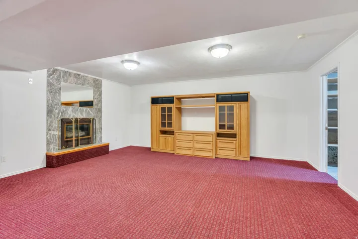 Basement: Spacious great room featuring a stone-surround gas fireplace with a brick hearth and a wood-finish media console