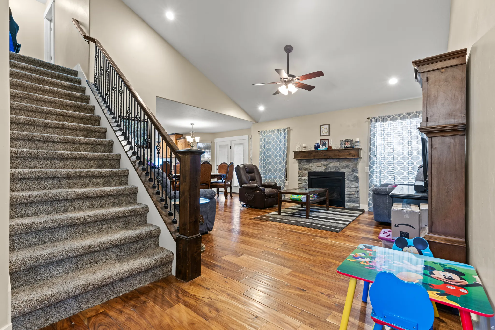 Open-concept living space with vaulted ceilings, a stone-front fireplace, and wood-finish flooring