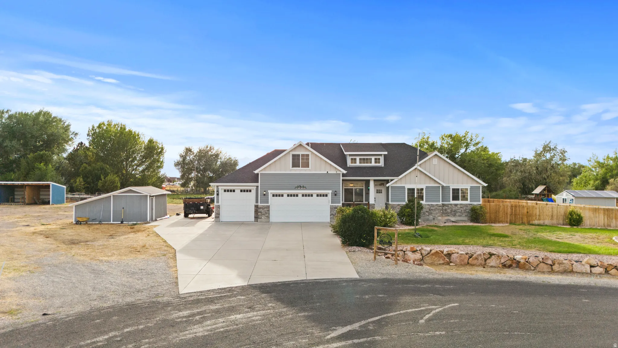 Modern farmhouse exterior featuring light blue siding, stone accents, two attached two-car garages, and a paved driveway
