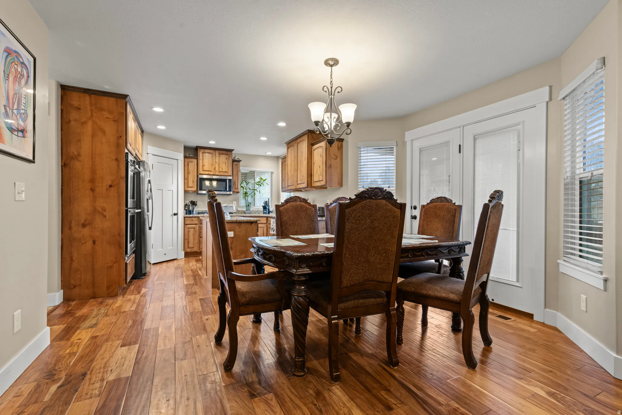 Hardwood flooring, wood cabinetry, built-in double ovens, recessed lighting, and a decorative chandelier