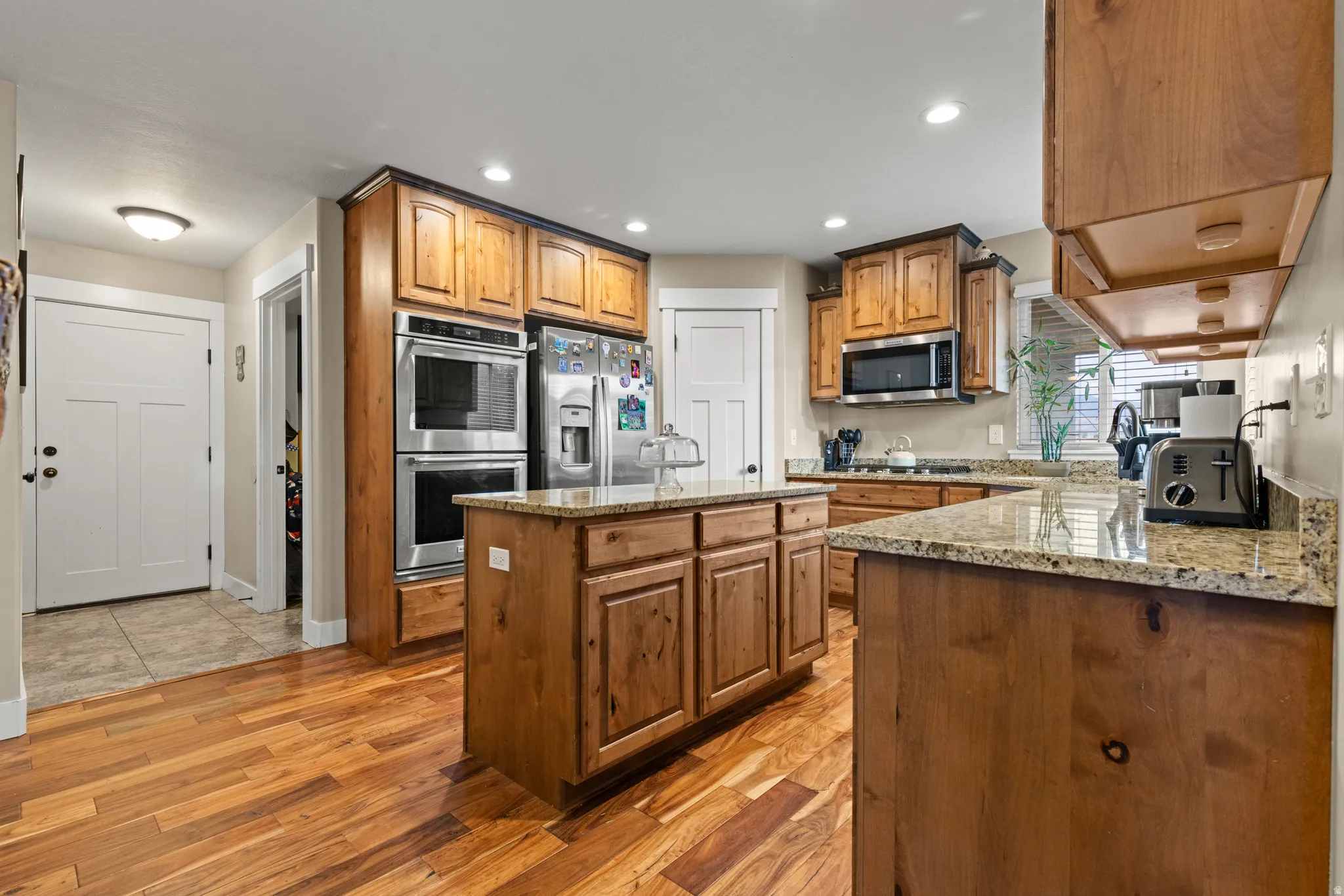 Kitchen featuring wood-finish flooring, recessed lighting, wood cabinetry, stone countertops, and stainless steel appliances