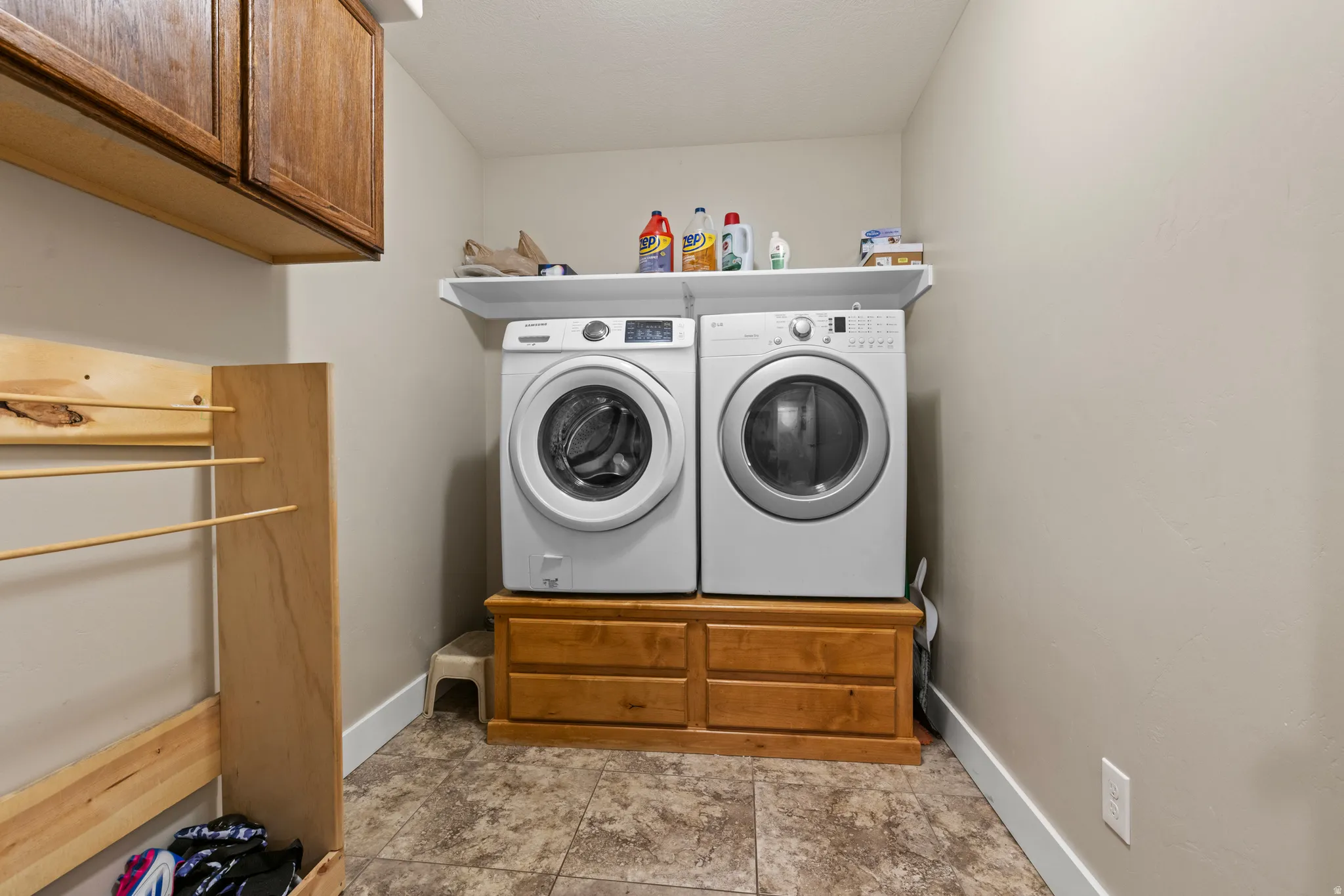 Laundry area featuring wood-finish cabinetry, a built-in wood-finish drying rack, a white wall shelf, and tiled flooring
