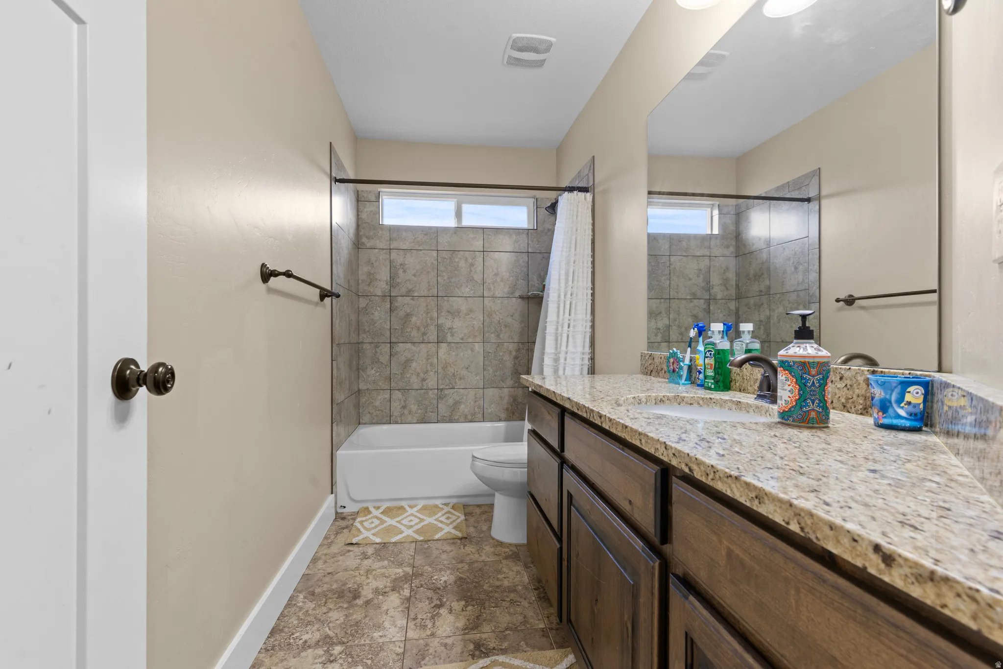 Bathroom featuring a sink with a granite-style countertop, a built-in tub with tile surround, and a rectangular window