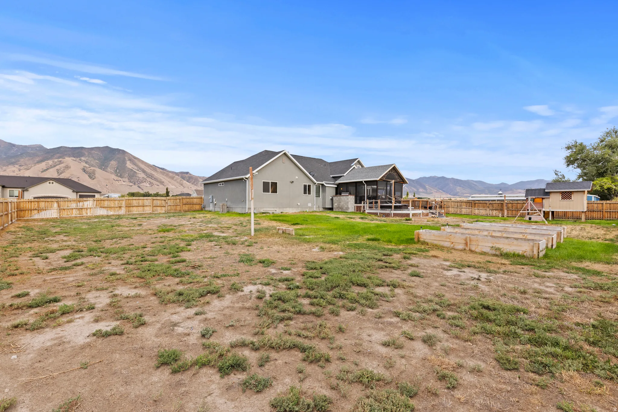 Expansive rear yard with a wood privacy fence, raised garden beds, and a screened-in porch