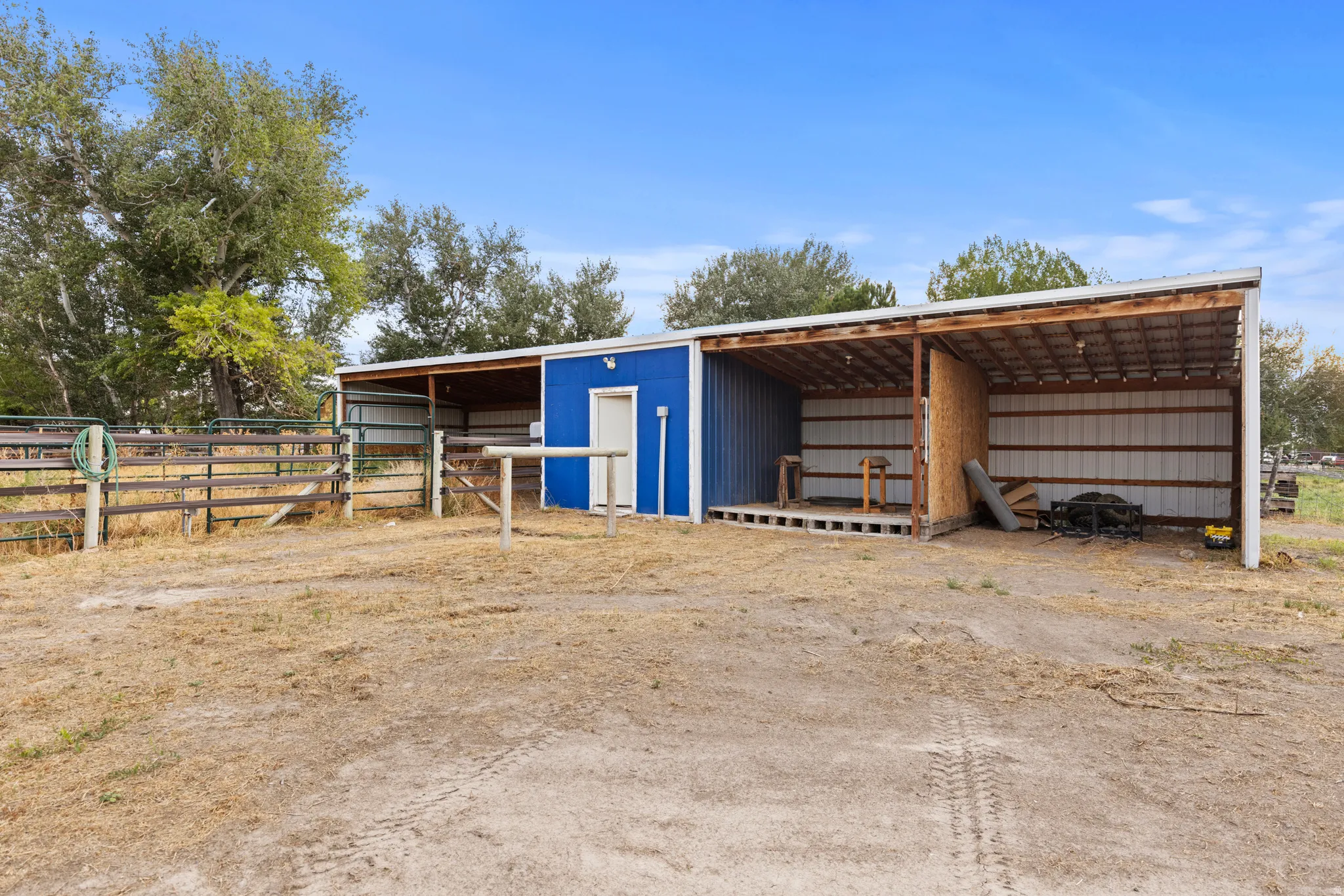 Metal-sided outbuilding with an attached lean-to structure, wood-framed overhang, and perimeter fencing.  2 horse corrals and 2 loafing sheds.  Hay storage.