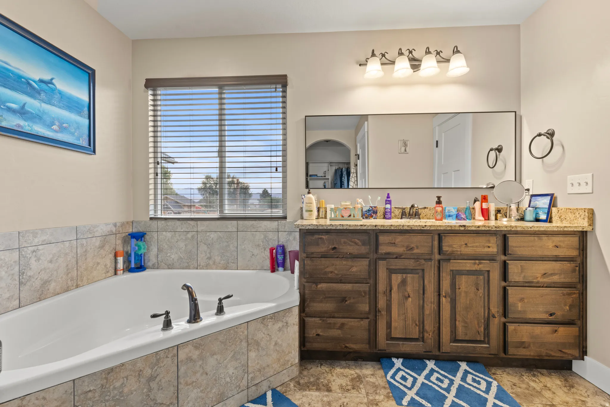 Built-in soaking tub with tile surround, vanity, and a large wall-mounted mirror