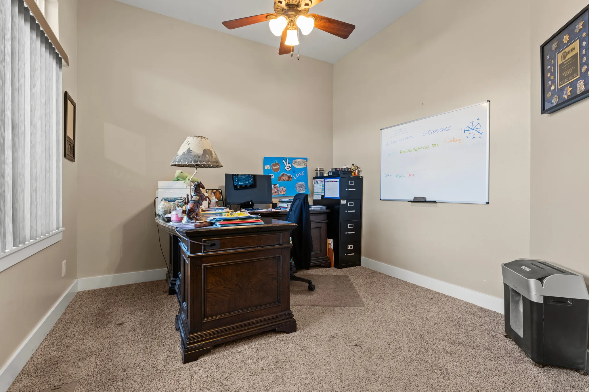 Neutral tone wall paint, vaulted ceiling, ceiling fan with light fixture, vertical window blinds, and carpet flooring