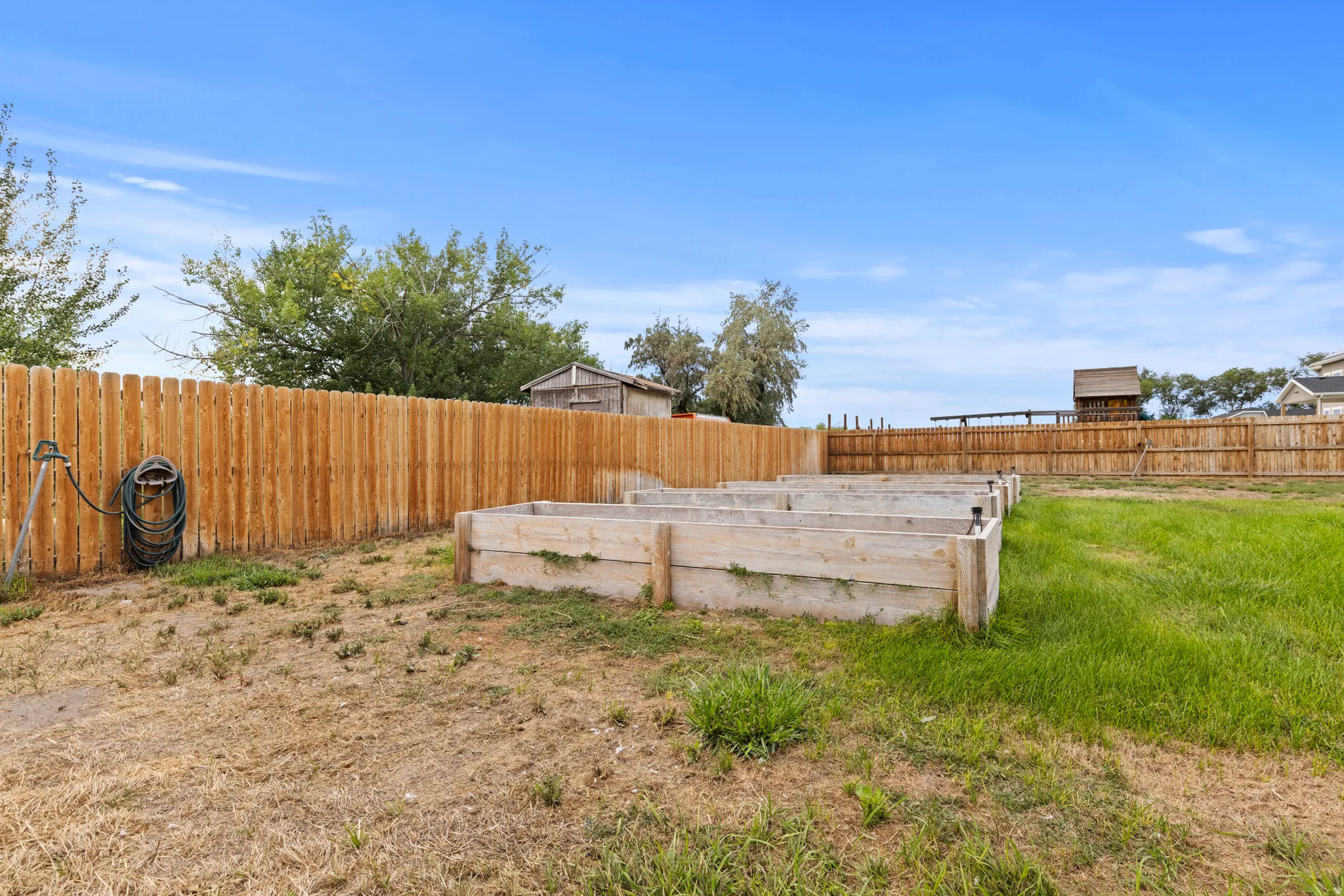 Expansive outdoor space featuring a wood privacy fence, multiple raised garden beds, and a combination of natural ground cover and grass