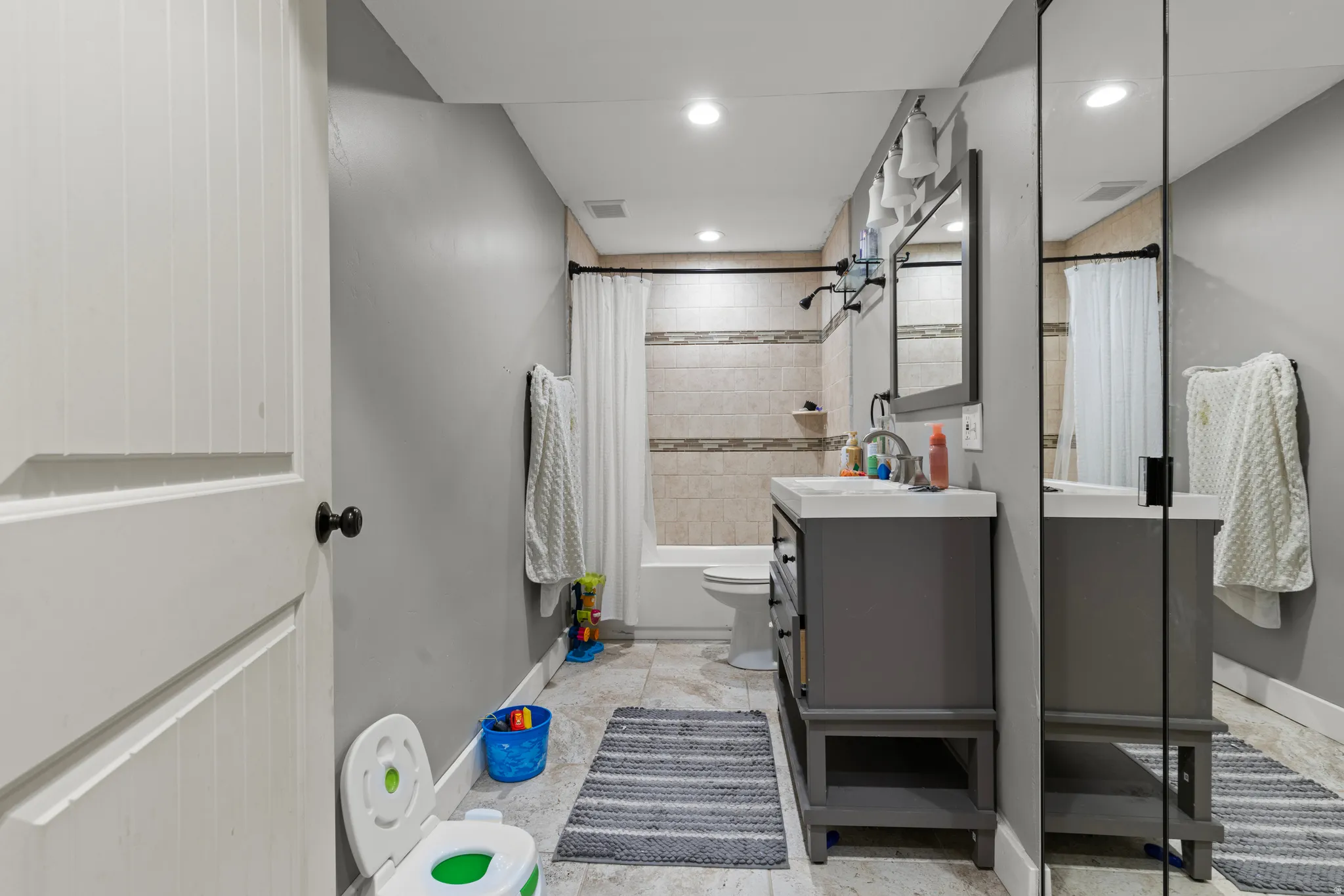 Full-length mirror closet, recessed ceiling lighting, light gray wall paint, tiled shower surround, and a vanity with an integrated sink