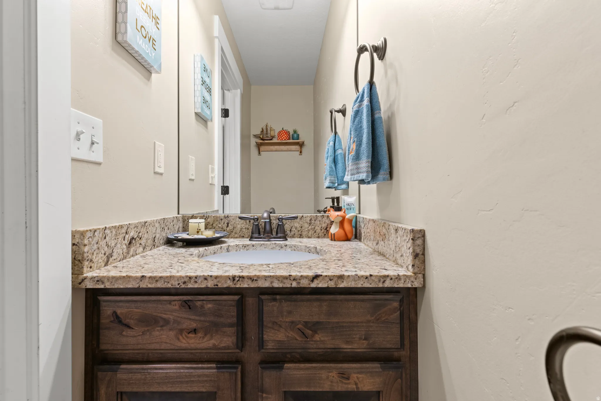 Granite countertop with an undermount sink, dark wood-finish vanity cabinetry, and a framed mirror
