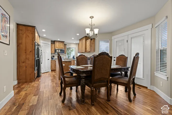 Hardwood flooring, wood cabinetry, built-in double ovens, recessed lighting, and a decorative chandelier
