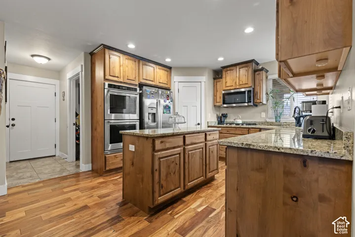 Kitchen featuring wood-finish flooring, recessed lighting, wood cabinetry, stone countertops, and stainless steel appliances