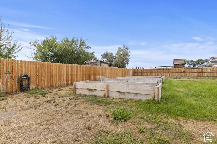 Expansive outdoor space featuring a wood privacy fence, multiple raised garden beds, and a combination of natural ground cover and grass