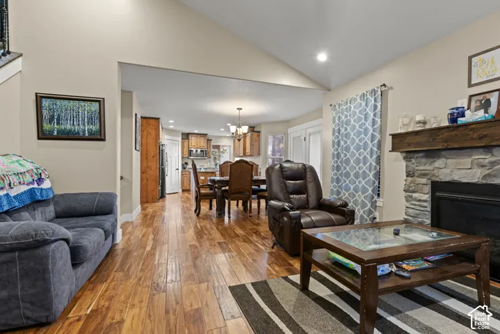 Vaulted ceiling, stone surround fireplace with wood mantle, wood-finish flooring, recessed lighting, and a defined dining area