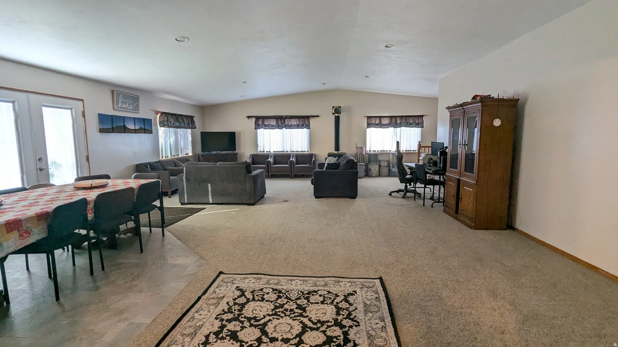 Spacious open-concept room featuring a wood-burning stove, multiple windows with blinds, a large dining area, and neutral wall paint
