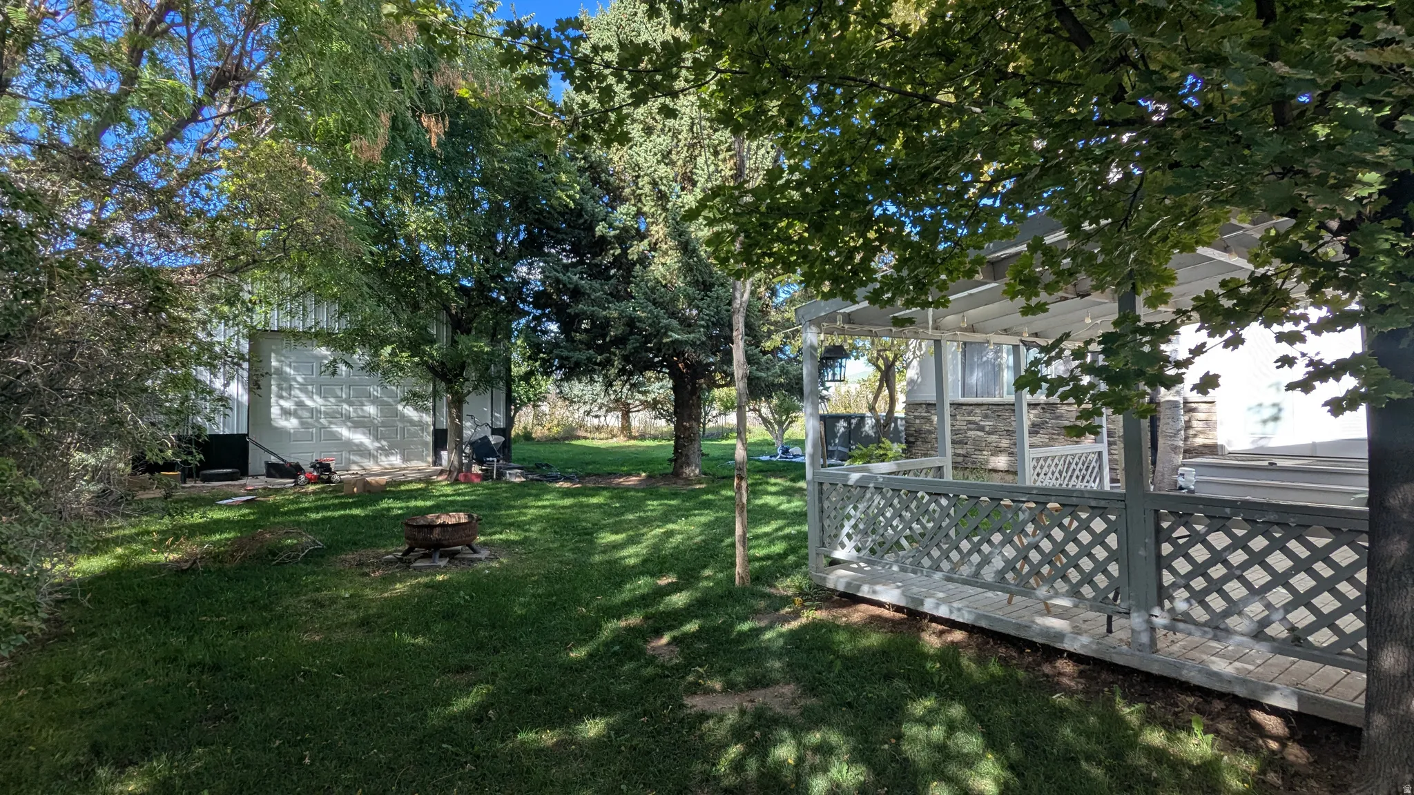 Expansive green lawn with mature trees, a covered patio featuring lattice railing, and a detached structure