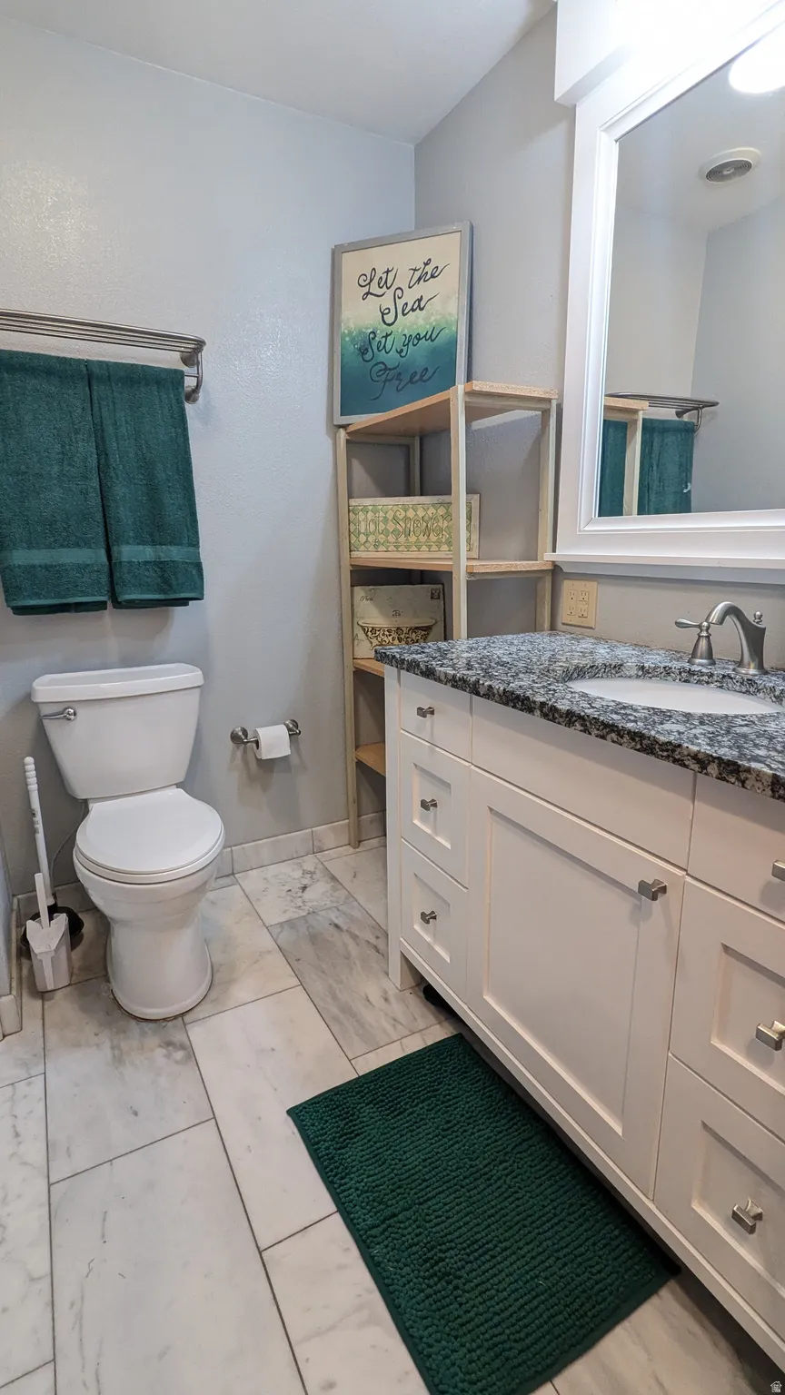 White vanity with a speckled countertop, a rectangular undermount sink, and brushed nickel hardware