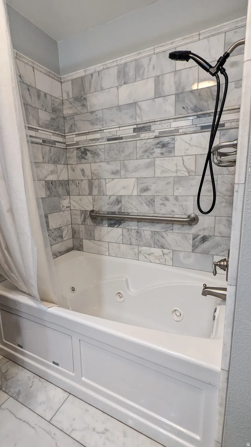 Soaking tub with integrated jets, subway tile surround, decorative mosaic tile accent, and brushed nickel fixtures