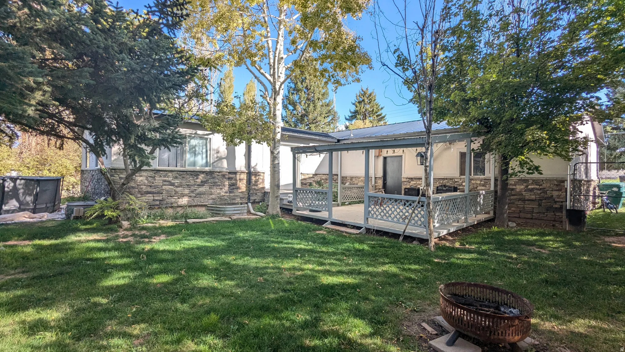 Expansive lawn with mature trees, a covered patio, and exterior stone accenting