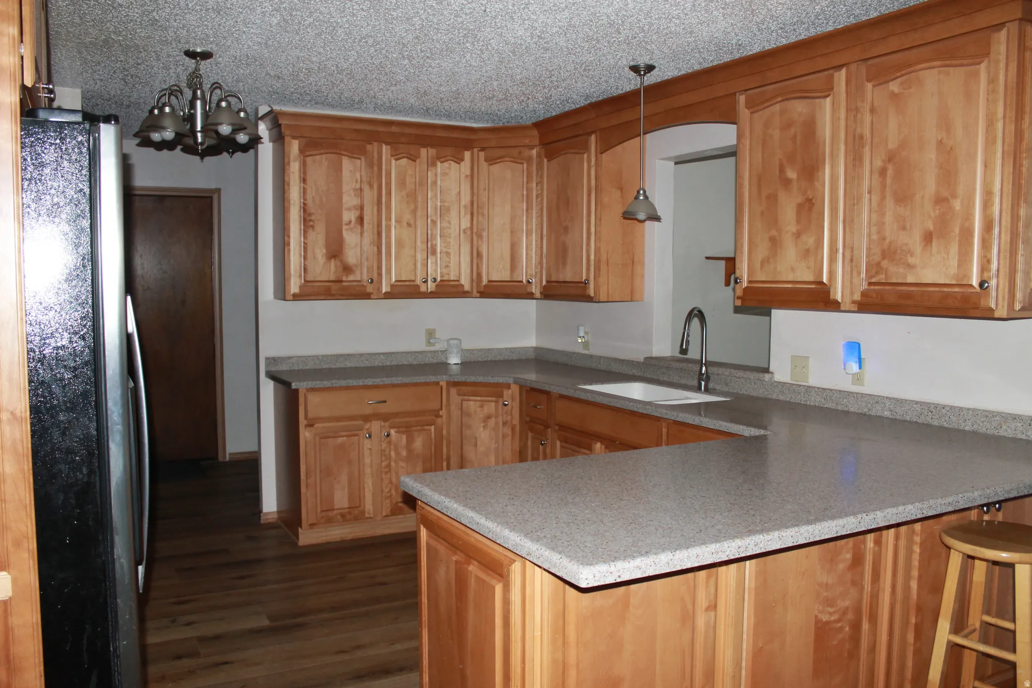U-shaped kitchen featuring wood-finish cabinetry, light-toned countertops, a stainless steel sink with a gooseneck faucet, and wood-finish flooring