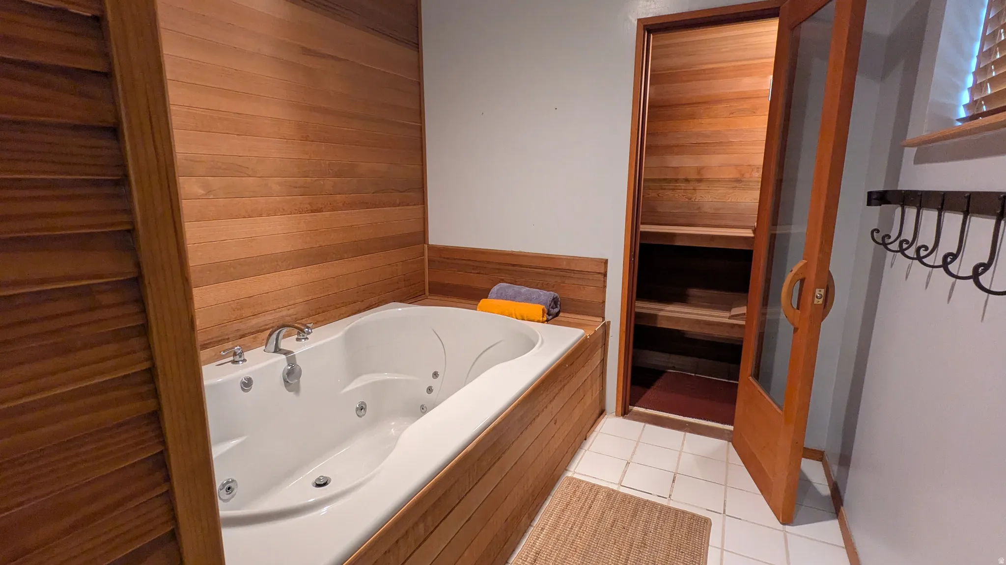 Jetted soaking tub with wood-paneled surround, wood-finish walls, and adjacent wood-paneled sauna with glass-paneled door