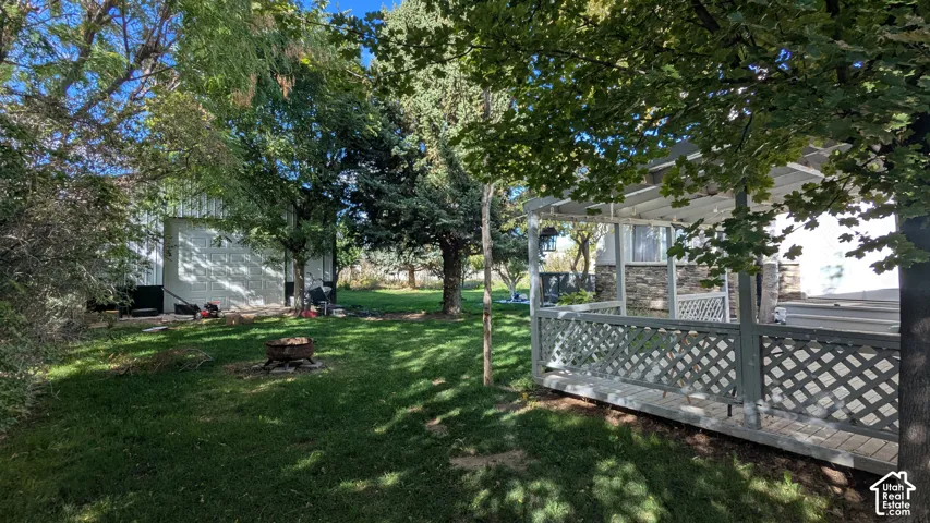 Expansive green lawn with mature trees, a covered patio featuring lattice railing, and a detached structure
