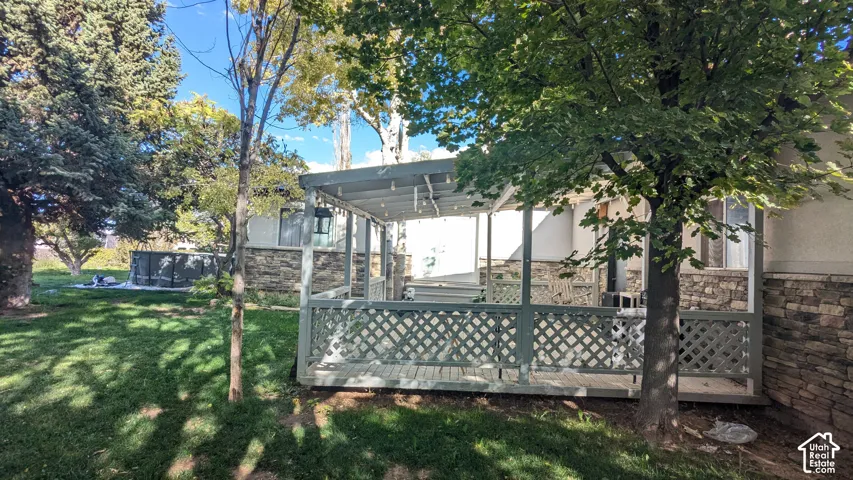 Covered deck with lattice railing, stone veneer foundation, and mature trees