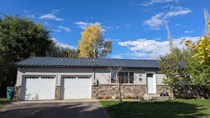 Two-car garage with white paneled doors, stone facade, light-colored exterior siding, and a dark metal roof