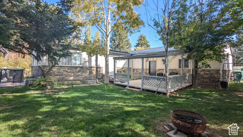 Expansive lawn with mature trees, a covered patio, and exterior stone accenting
