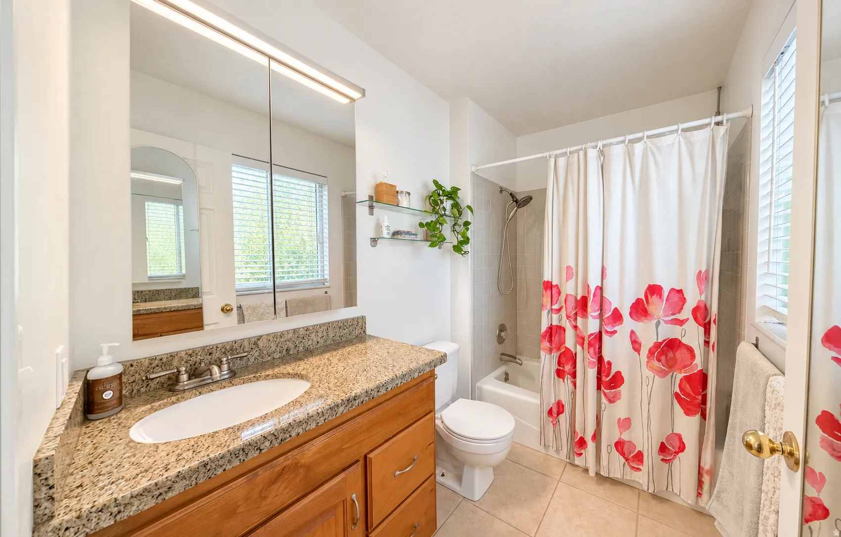 Bathroom featuring a wood vanity with a stone countertop, an integrated sink, a medicine cabinet with overhead lighting, and a shower-over-tub combination with a tiled surround
