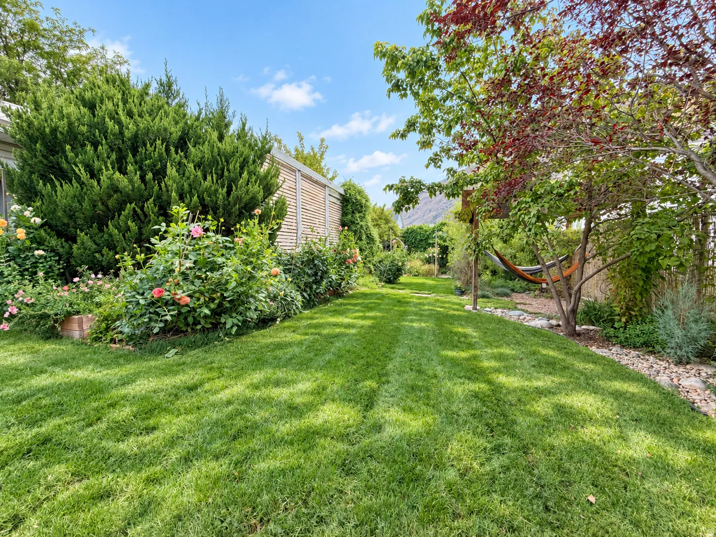 Expansive lawn area with manicured grass, vibrant mature landscaping, and an architectural wood fence