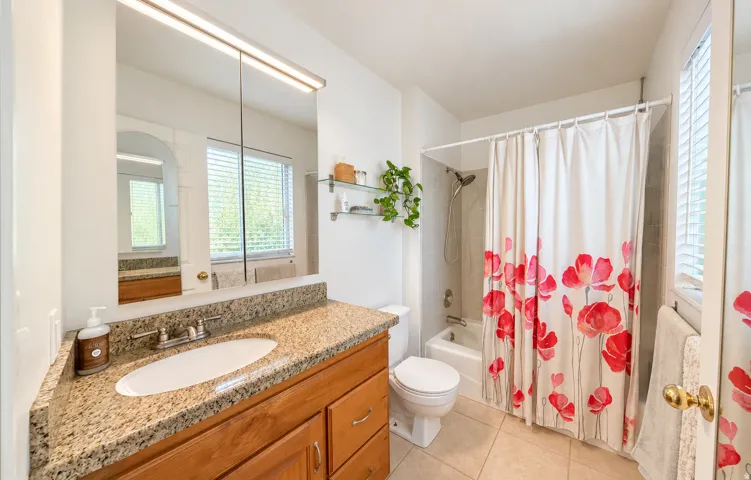 Bathroom featuring a wood vanity with a stone countertop, an integrated sink, a medicine cabinet with overhead lighting, and a shower-over-tub combination with a tiled surround