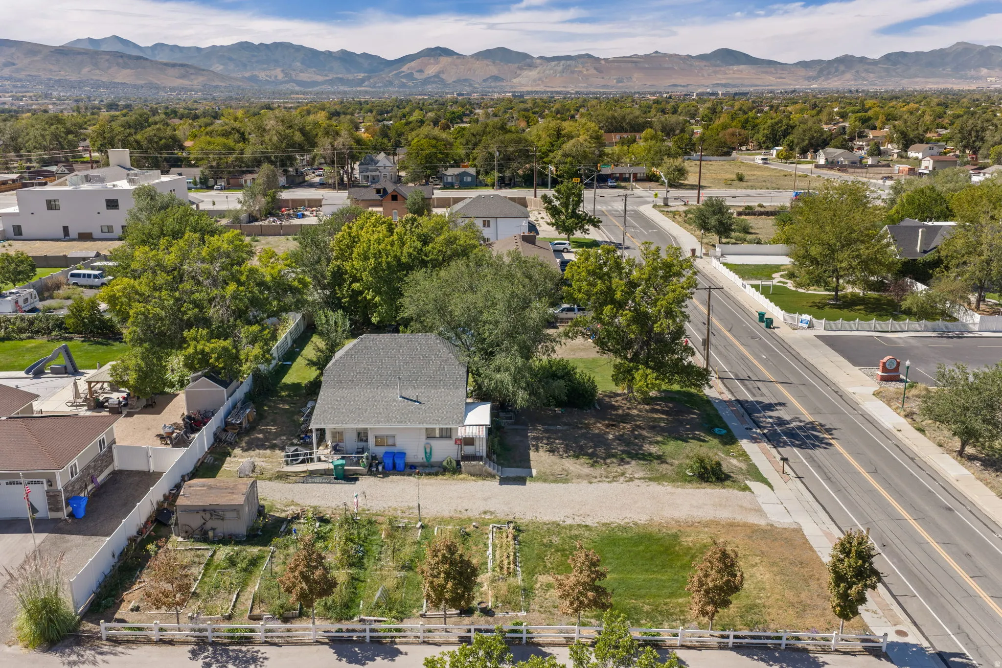 Expansive lot featuring a single-story residence with a gray shingle roof, a detached shed, a white privacy fence, and a garden area