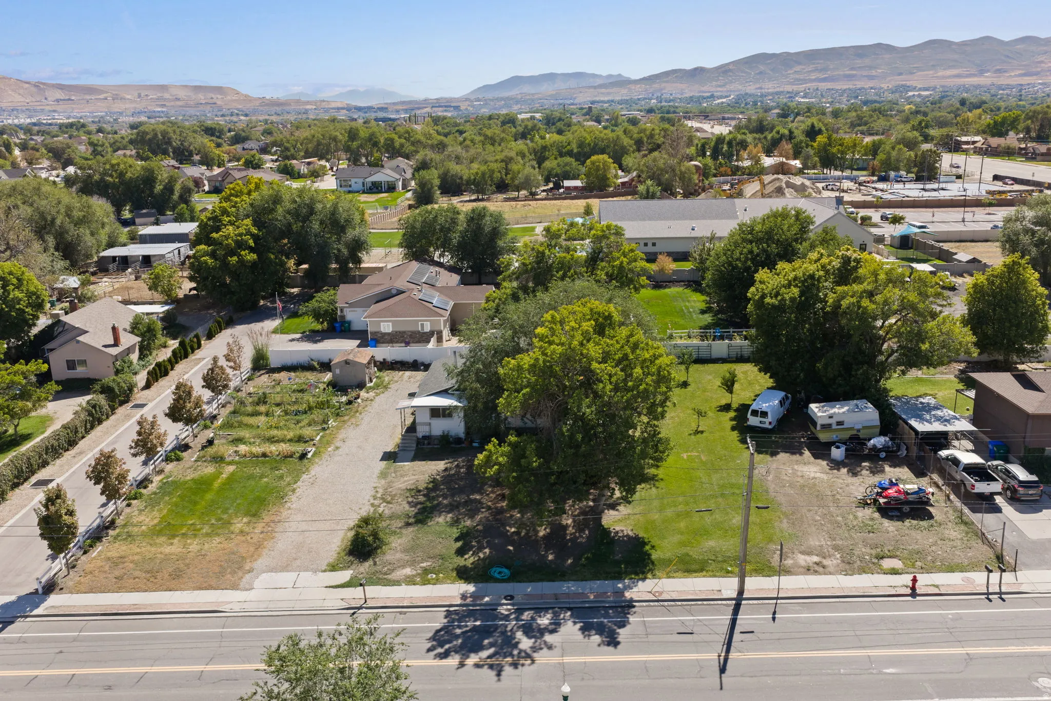 Expansive lot featuring a paved roadway, established trees, and surrounding neighborhood with mountainous backdrop