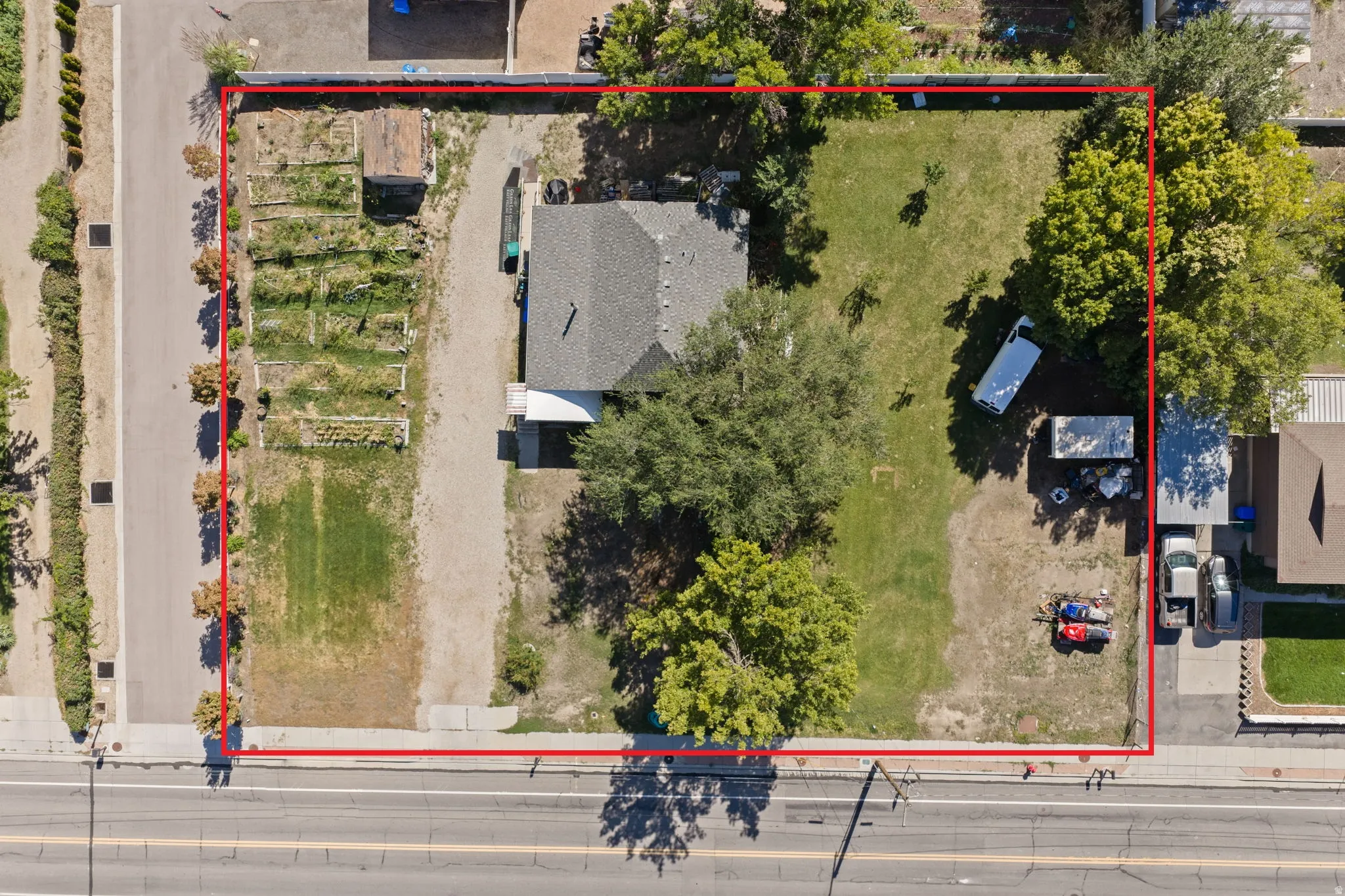 Expansive lot featuring a residential structure, mature trees, designated garden beds, and direct road frontage