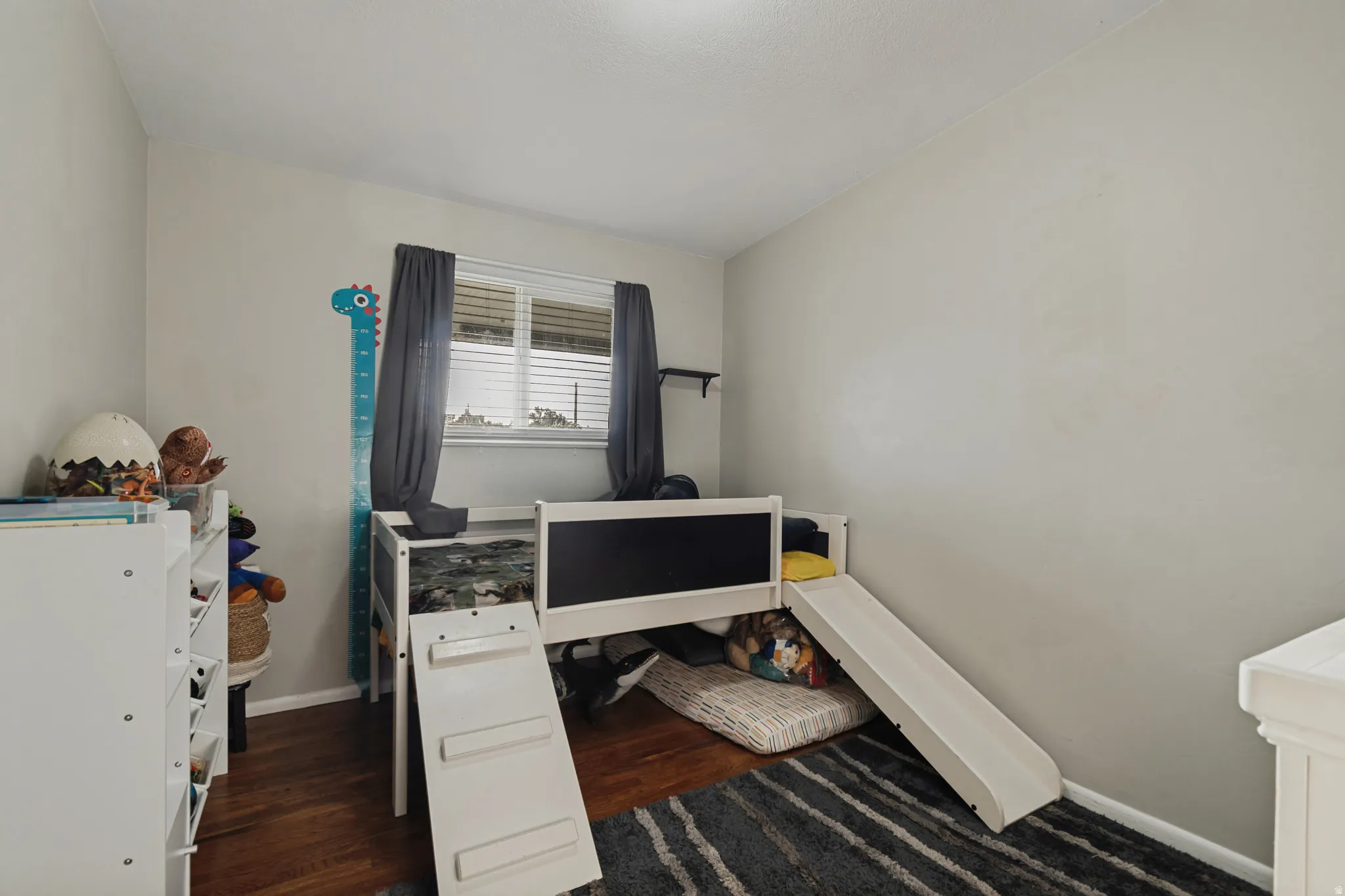 Wood-finish flooring, neutral wall color, and a window with blinds