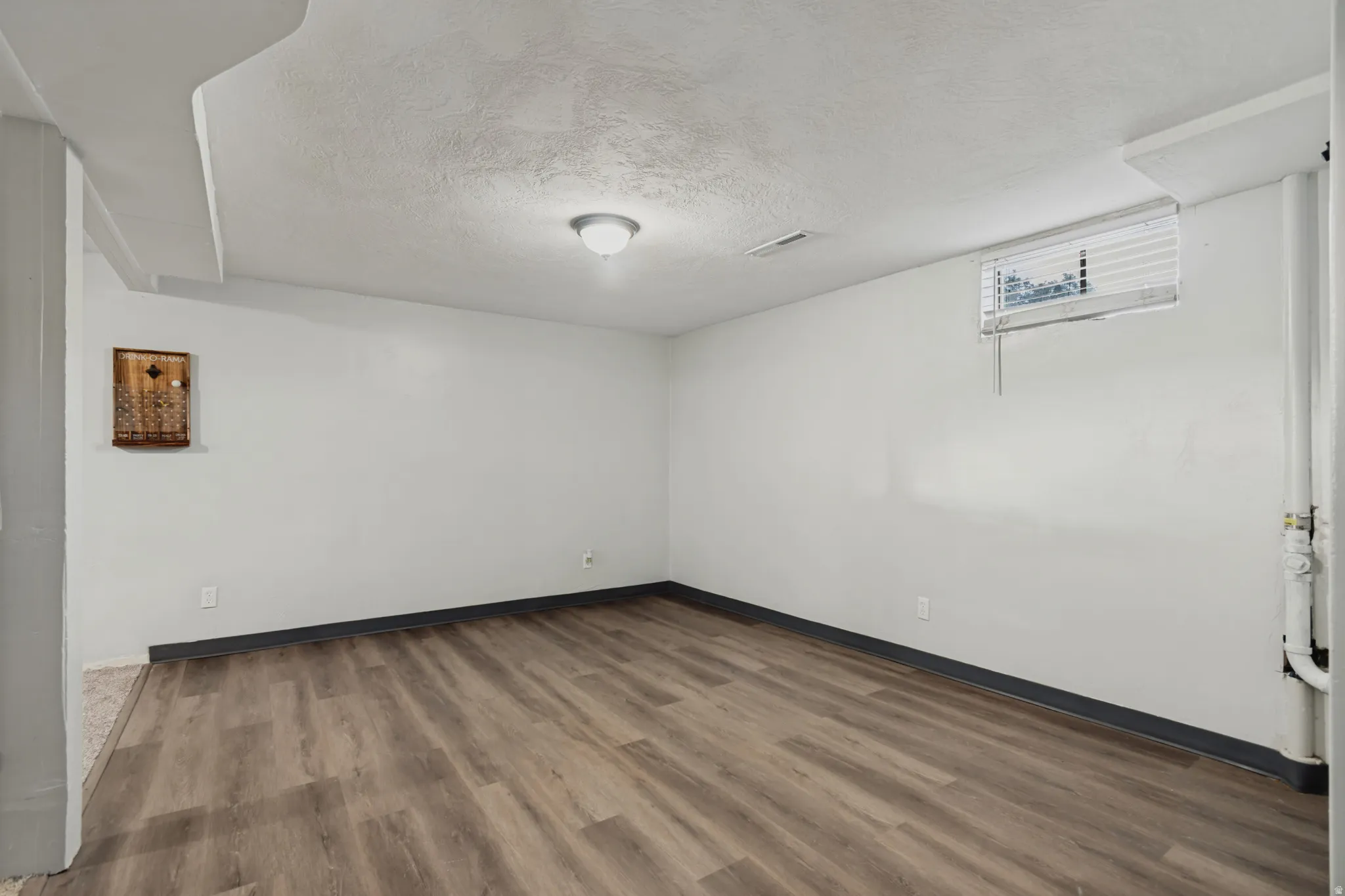 Wood-finish flooring with coordinating baseboards, recessed window with blinds, and ceiling-mounted light fixture