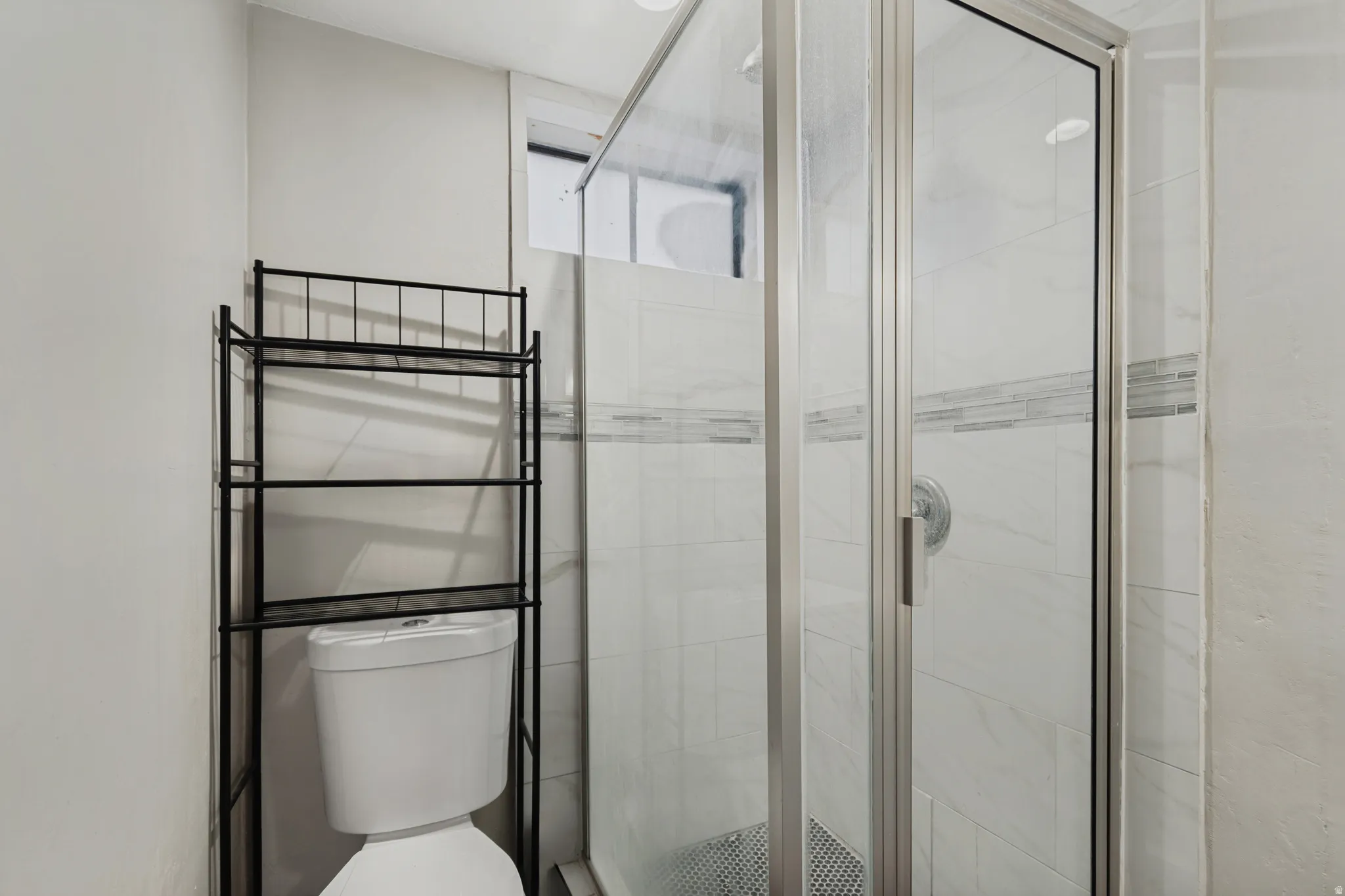 Glass-enclosed shower with a tiled surround, accent tile band, and polished chrome fixtures