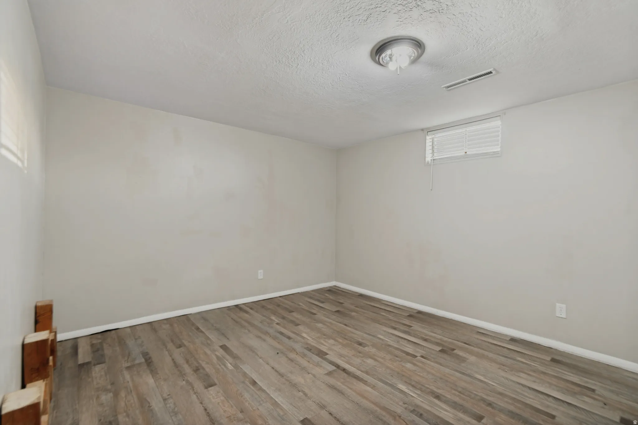 Wood-finish flooring with white baseboards, a flush-mount ceiling light, and a window with blinds