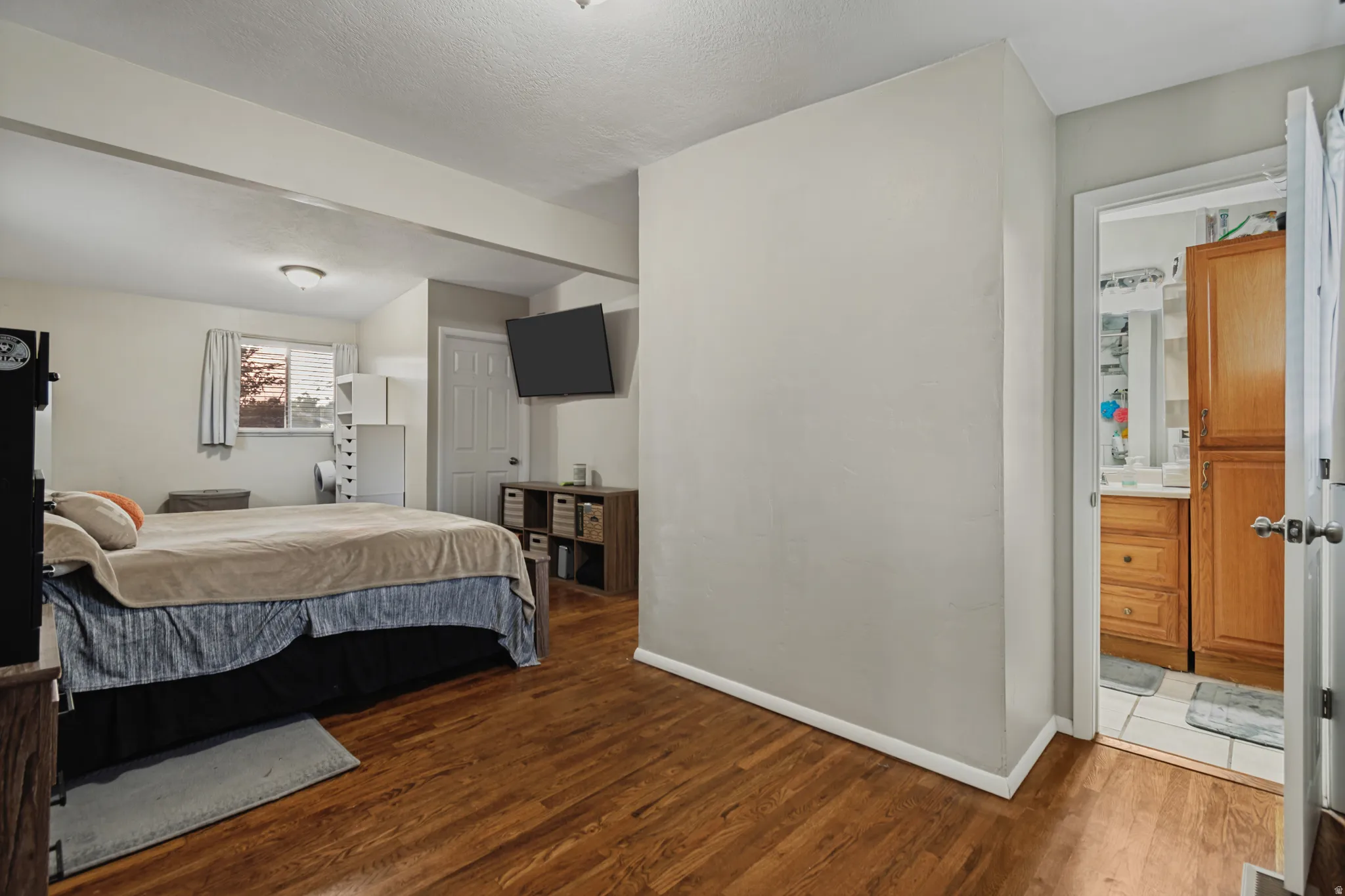 Wood-finish flooring throughout, ceiling-mounted light fixtures, built-in shelving, and an adjacent bathroom with wood cabinetry