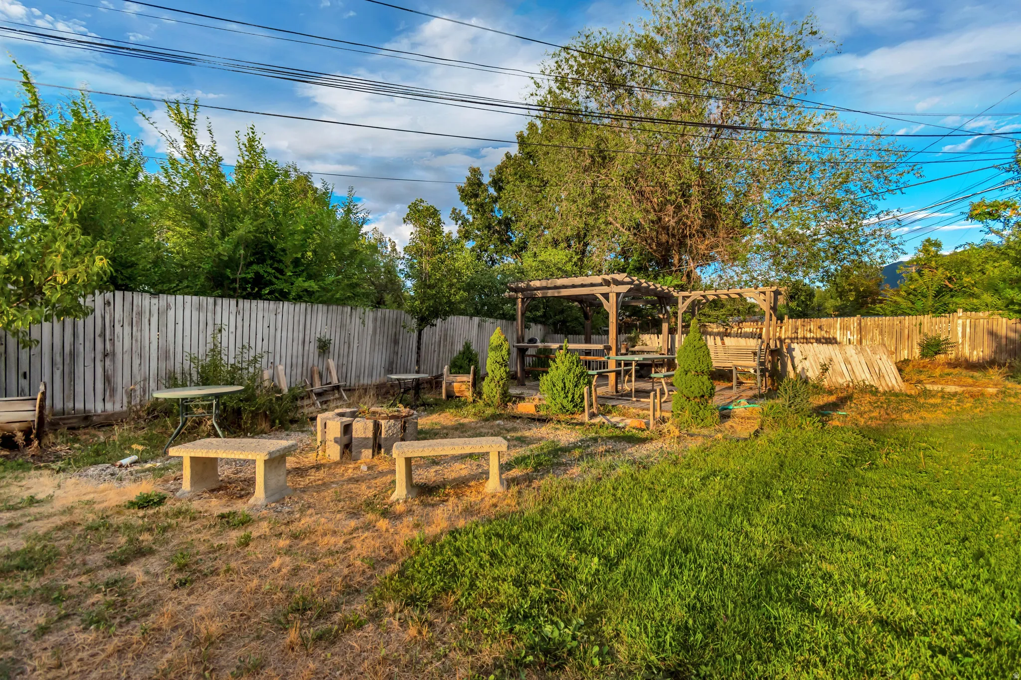 Expansive yard featuring a wooden privacy fence, a built-in pergola structure, and a designated fire pit area