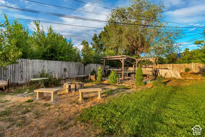 Expansive yard featuring a wooden privacy fence, a built-in pergola structure, and a designated fire pit area