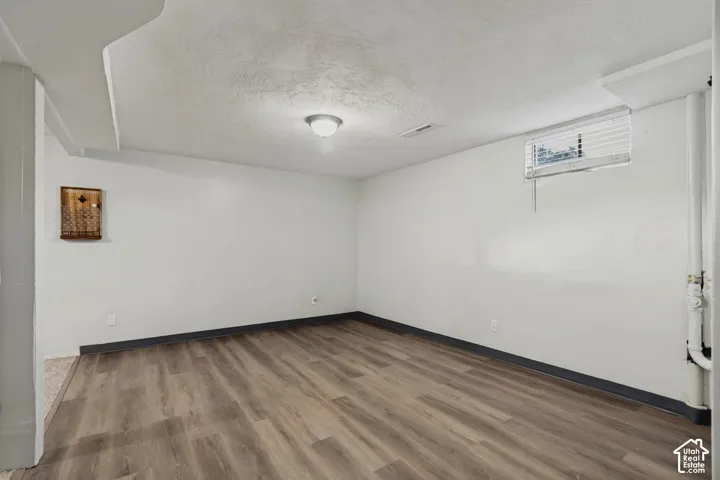 Wood-finish flooring with coordinating baseboards, recessed window with blinds, and ceiling-mounted light fixture