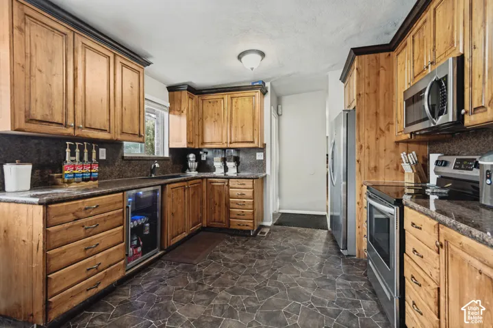 Wood-finish cabinetry with contrasting trim, stone-finish countertops, stainless steel appliances, and a built-in beverage refrigerator