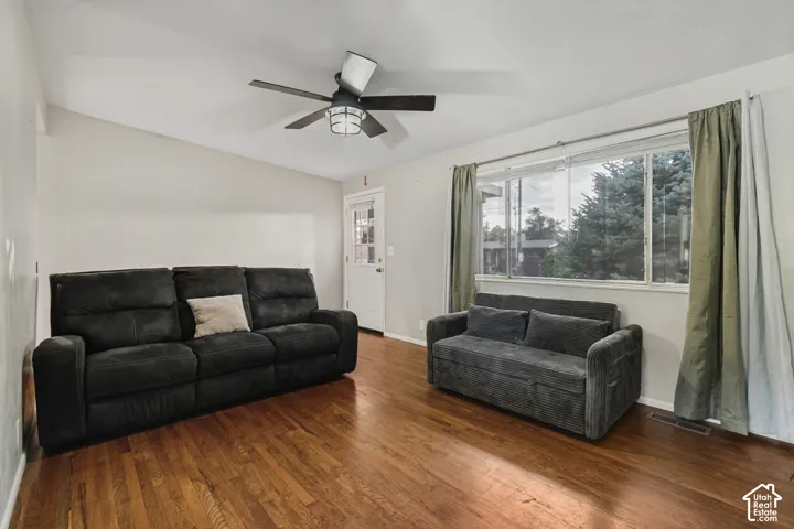 Wood-finish flooring, white walls, large window, ceiling fan with integrated lighting, and a white paneled door
