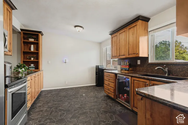 Custom wood cabinetry with dark crown molding, stone-finish flooring, stainless steel range, built-in beverage cooler, and dark stone countertops